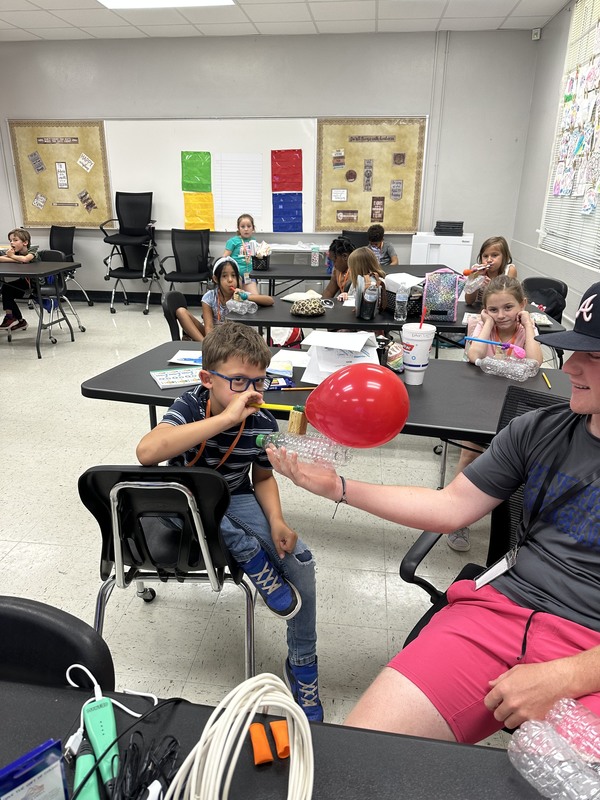 A camper demonstrates the balloon-powered boat he made.